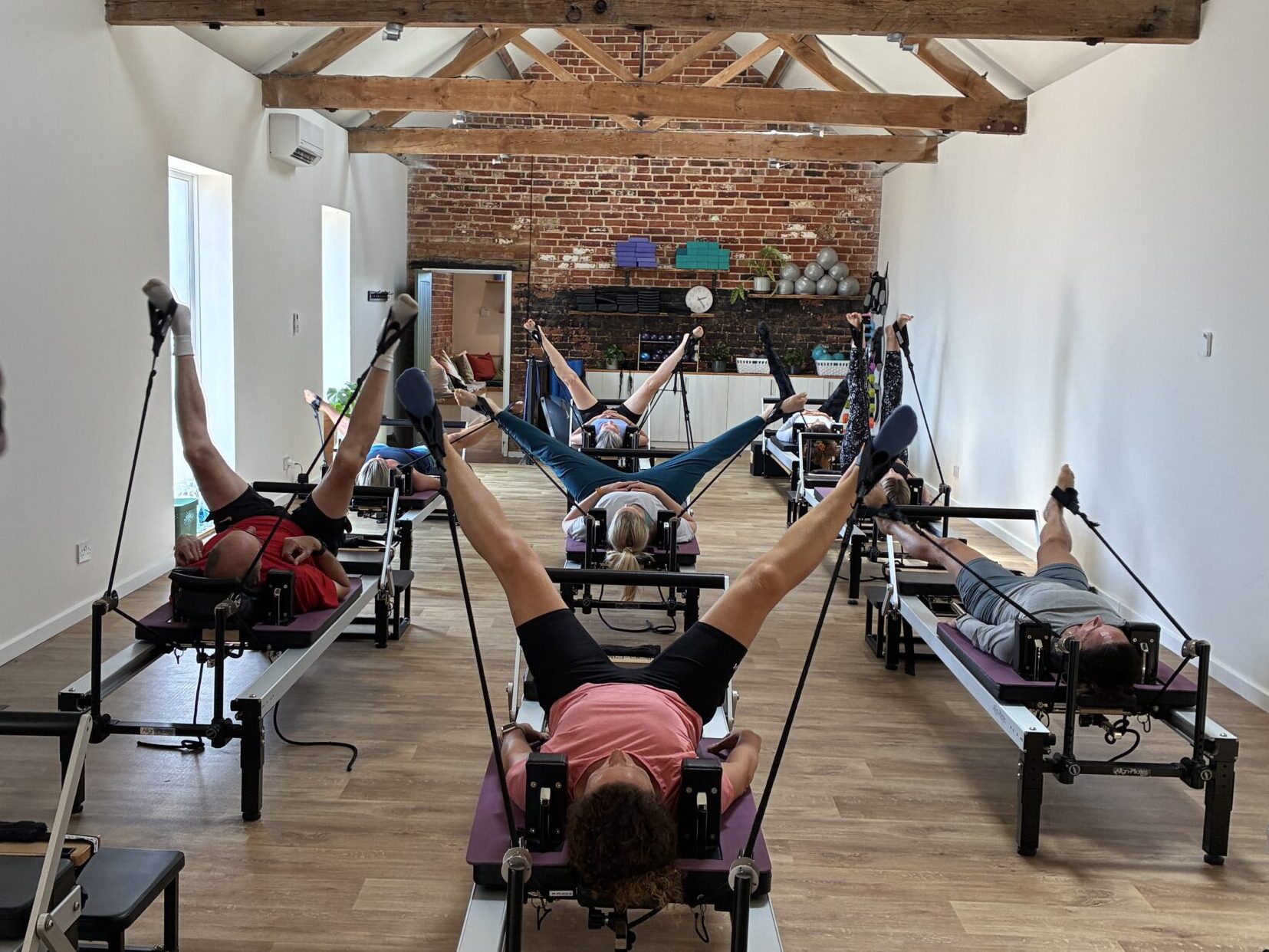 A group of people laying on reformer beds with legs outstretched in the reformer studio at Cottesloe Physio, Wing